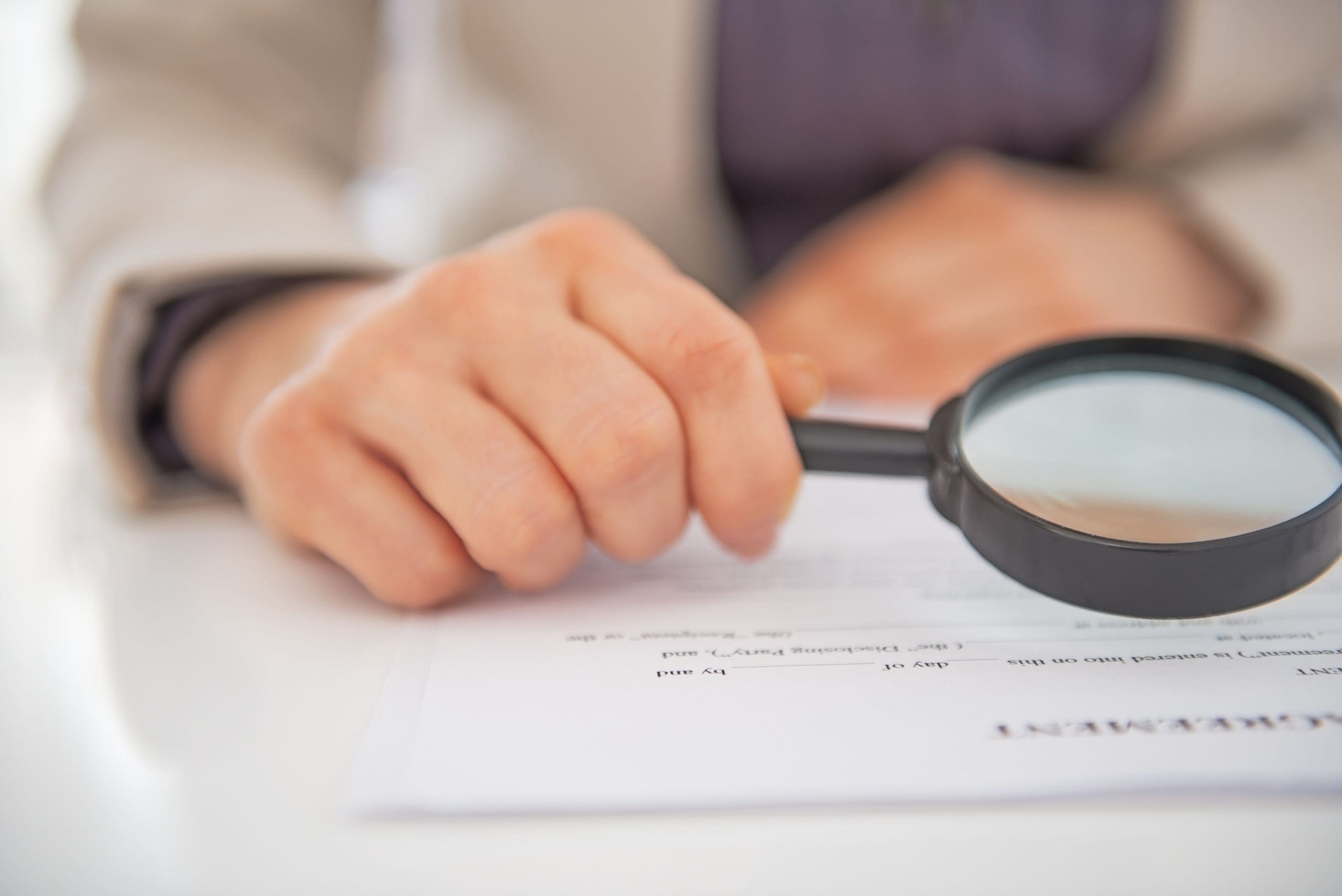 A person looking at a document with a magnifying glass.