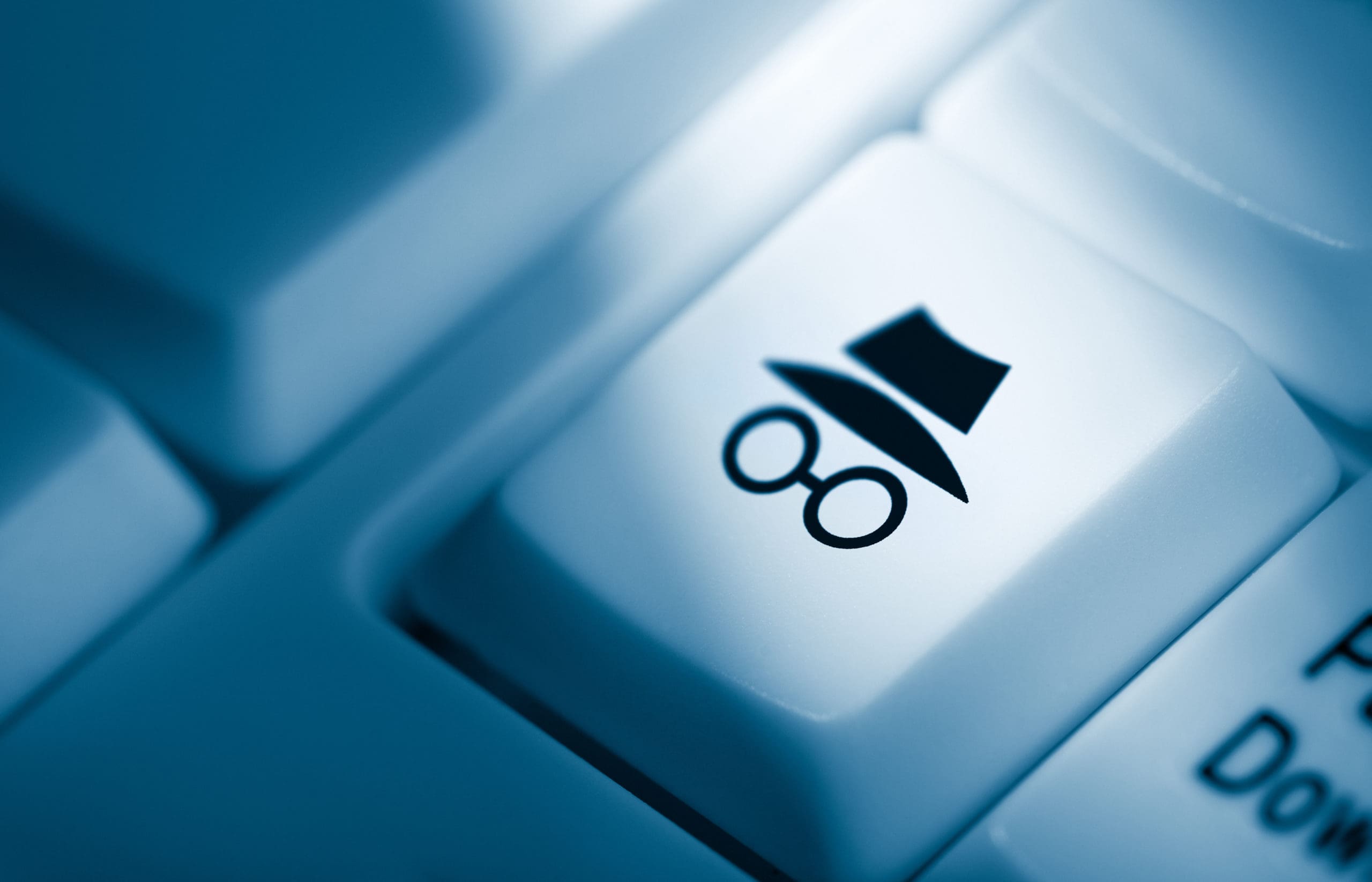 A close-up view of a keyboard key adorned with the symbol of a top hat and a pair of round spectacles, suggesting a quirky or specialized function, in a cool blue monochromatic light.