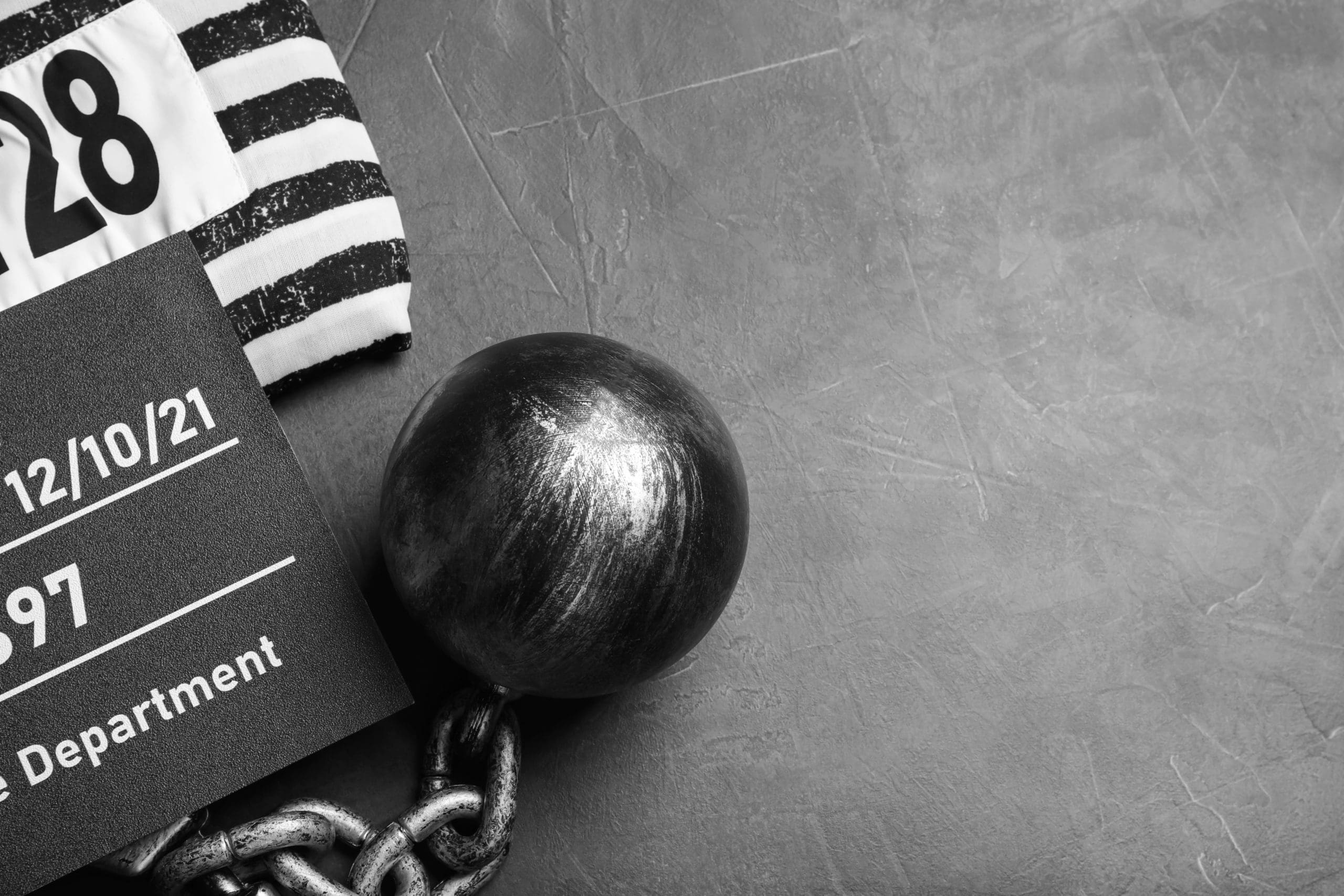 Monochrome image depicting a vintage convict theme with striped prisoner uniform, a ball and chain, and a booking date card.